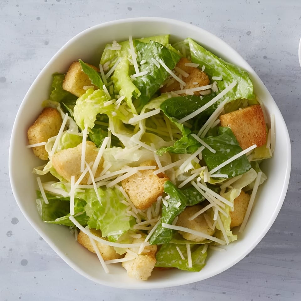 Caesar salad with crisp romaine lettuce, crunchy croutons, and shredded Parmesan cheese in a white bowl.