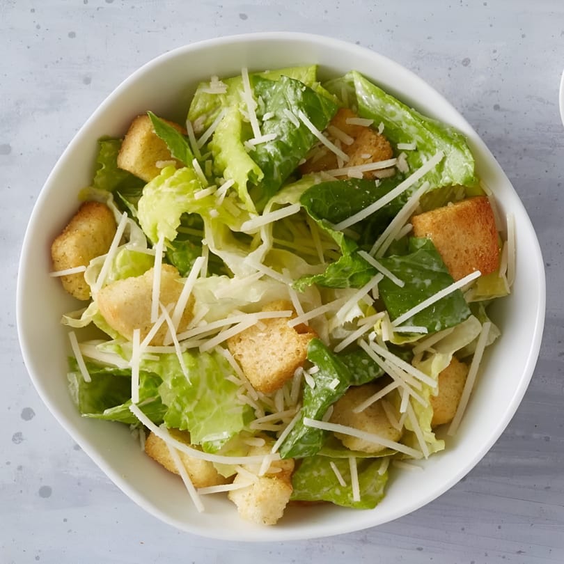 Caesar salad with crisp romaine lettuce, crunchy croutons, and shredded Parmesan cheese in a white bowl.