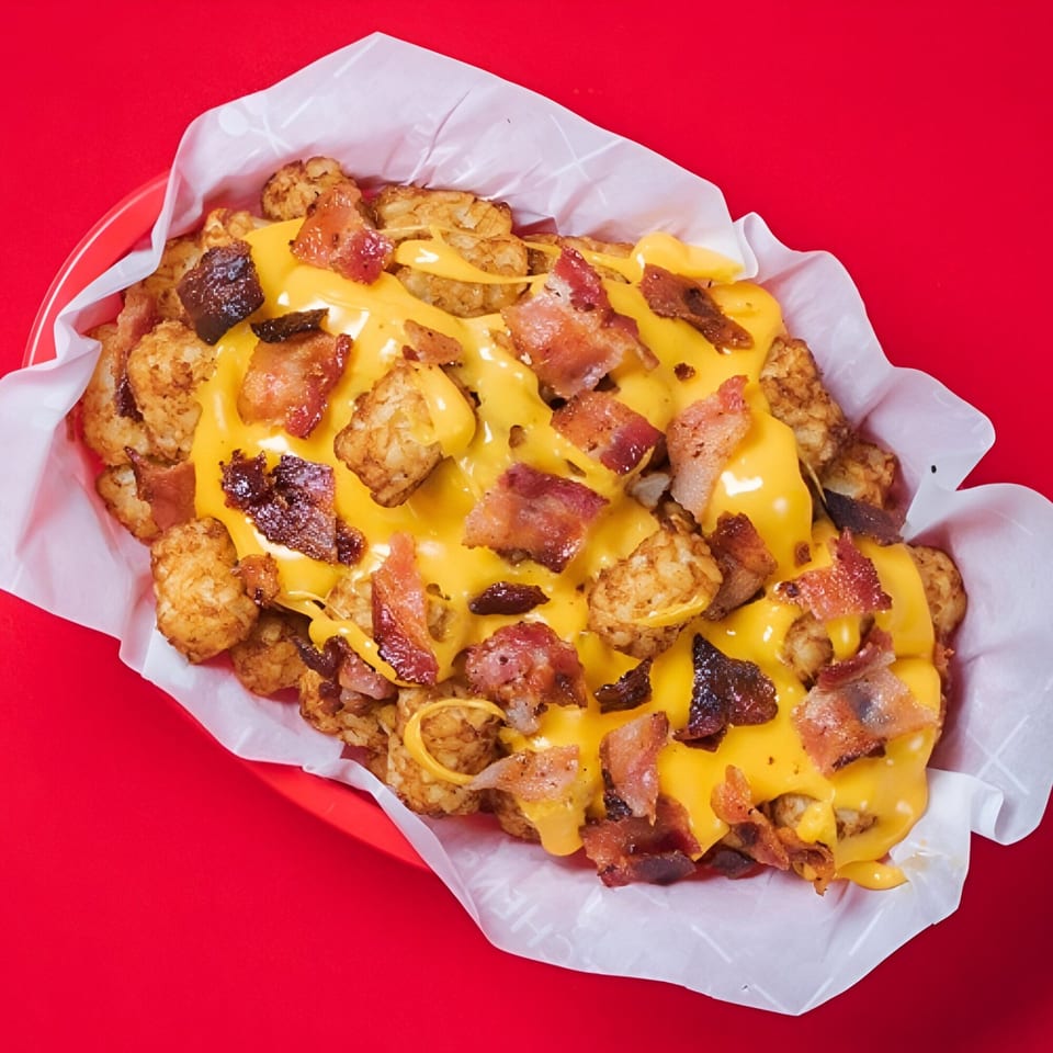 Loaded tater tots with melted cheese and crispy bacon bits in a red basket.