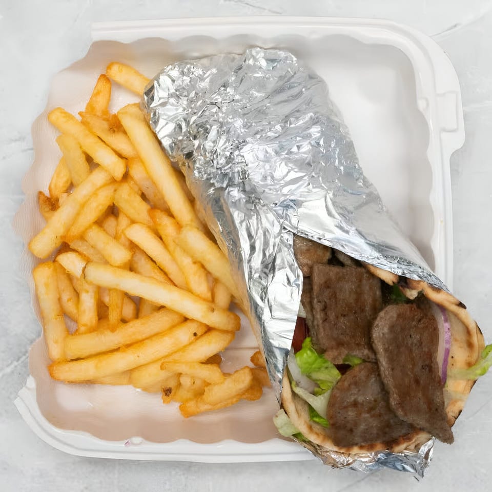 A gyro with meat, lettuce, and onions, wrapped in foil, next to a pile of french fries.